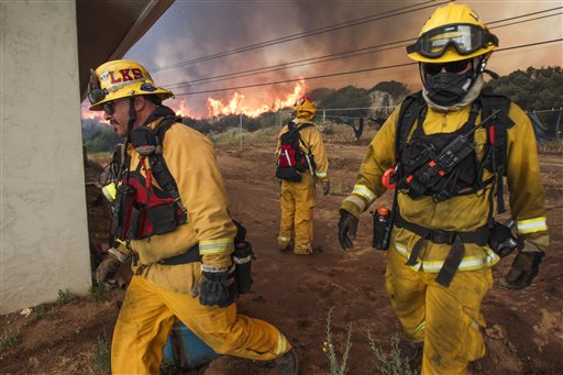 Lakeside firefighters Joe Vasquez, left, and David Csik walk around a house as Lakeside Fire Capt. Jon Jordan watches large flames burn toward the home on Highway 94 south of Potrero Calif., on Monday, June 20, 2016. An intensifying heat wave stretching from the West Coast to New Mexico threatened to make the fight against Southern California wildfires more difficult Monday. (Hayne Palmour IV/San Diego Union-Tribune via AP)