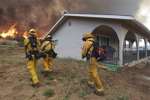 Lakeside firefighters walk next to a home on Highway 94 south of Potrero, Calif., as a wildfire burns near the home on Monday, June 20, 2016. An intensifying heat wave stretching from the West Coast to New Mexico threatened to make the fight against Southern California wildfires more difficult Monday. (Hayne Palmour IV/San Diego Union-Tribune via AP)