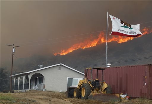 The California state flag flies next to a home on Highway 94 south Potrero, Calif., on Monday, June 20, 2016, as huge flames roar behind it. An intensifying heat wave stretching from the West Coast to New Mexico threatened to make the fight against Southern California wildfires more difficult Monday. (Hayne Palmour IV/San Diego Union-Tribune via AP)