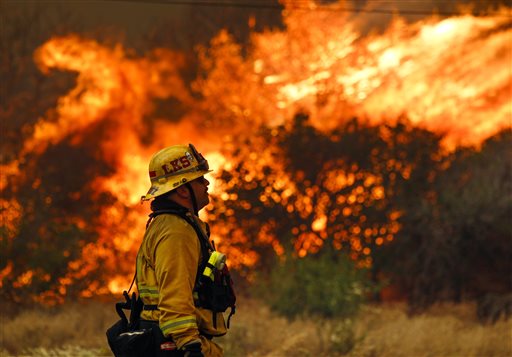 Lakeside firefighter Joe Vasquez watches as large flames burn next to a home on Highway 94 south of Potrero, Calif., on Monday, June 20, 2016. An intensifying heat wave stretching from the West Coast to New Mexico threatened to make the fight against Southern California wildfires more difficult Monday. (Hayne Palmour IV/San Diego Union-Tribune via AP)